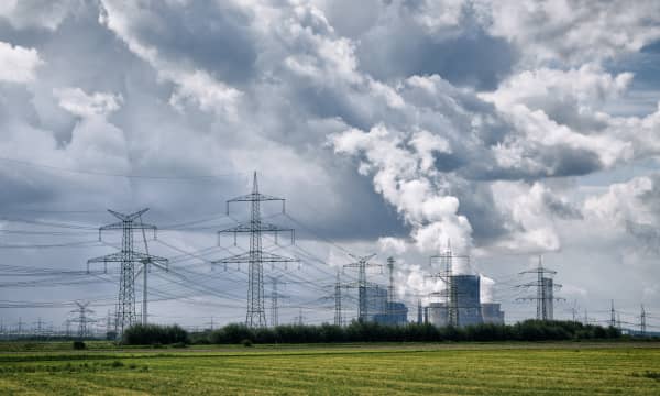 Laufendes Kraftwerk und Strommasten mit grüner Wiese im Vordergrund