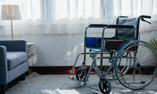 Rollstuhl auf einem Teppich neben einem blauen Sessel vor einem Fenster