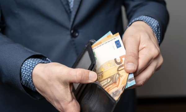 Älterer Mann im Anzug öffnet eine Geldbörse mit mehreren Geldscheinen