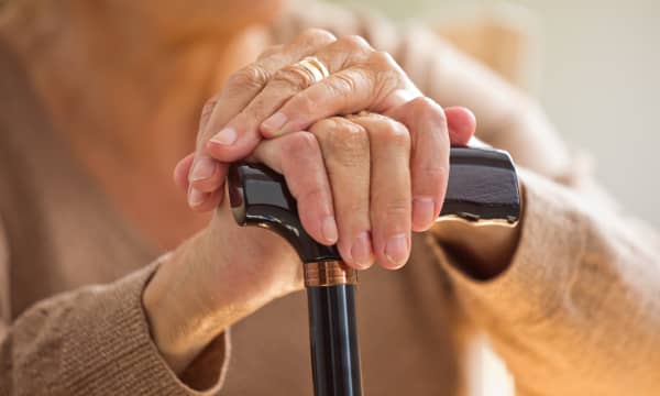 Seniorin hält einen Gehstock fest, der Fokus liegt auf ihren Händen