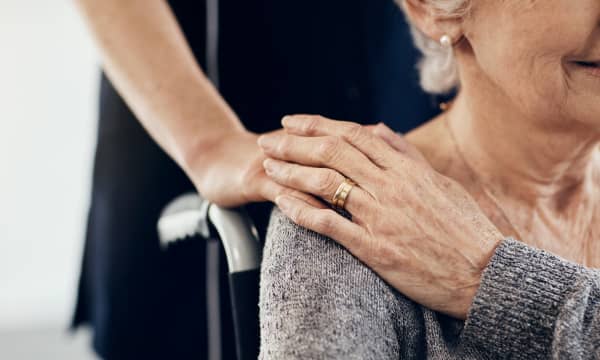 Junge Frau legt eine Hand auf die Schulter einer Seniorin in einem Rollstuhl