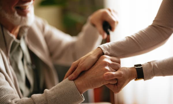 Sitzender Senior und jüngere stehende Frau mit Fokus auf den Händen