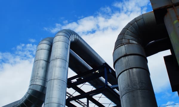 Fernwärmeleitungen in einem Blockheizkraftwerk unter blauem, leicht bewölktem Himmel
