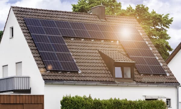 Wohnhaus mit weißer Fassade, brauner Dacheindeckung und Solarmodulen, auf die die Sonne scheint