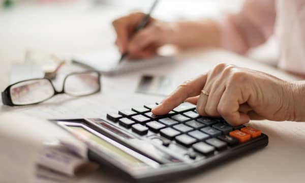 Nahaufnahme der Hände einer älteren Frau, die auf einem Taschenrechner tippt