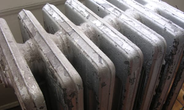 Alter Gliederheizkörper mit abgeplatzter Farbe in einem Wohnraum