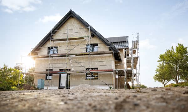 Haus mit Gerüst auf unbepflanztem Boden bei blauem Himmel