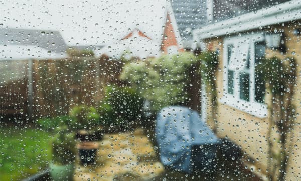 Blick aus einem Wohnhaus nach draußen aus einem Fenster, das mit Regentropfen bedeckt ist