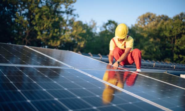 Monteur mit roter Arbeitshose und gelbem Helm montiert eine Solaranlage auf dem Dach
