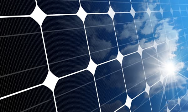 Nahansicht eines Solarmoduls, auf das die Sonne scheint, der leicht bewölkte Himmel spiegelt sich darin