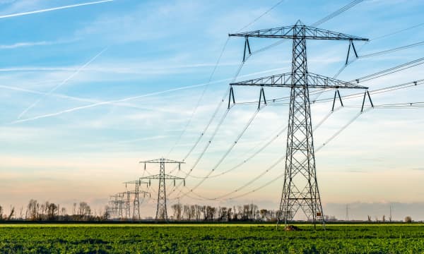 Strommasten auf grüner Wiese bei leicht bewölktem Himmel