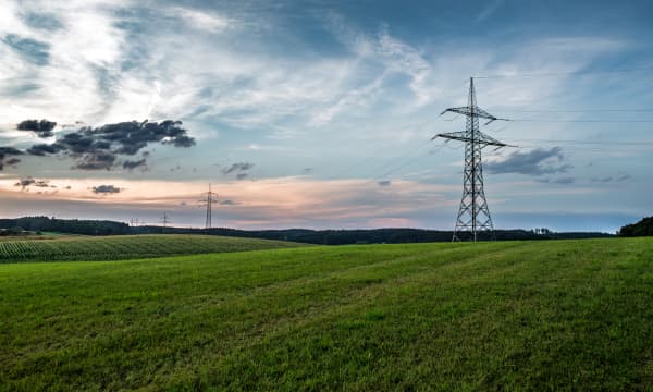 Strommasten auf grüner Wiese vor bewölktem Himmel