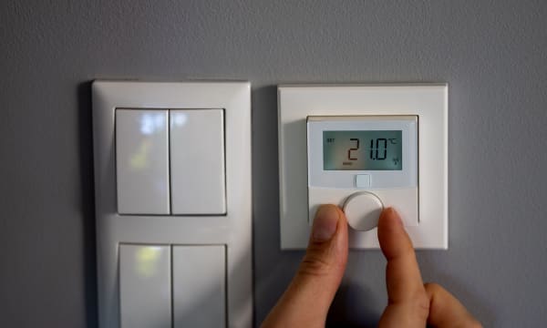 Lichtschalter und digitales Heizungsthermostat an der Wand. Eine Hand regelt die Temperatur.