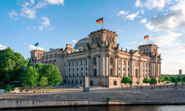 Seitenansicht des Reichstagsgebäudes in Berlin mit blauem, leicht bewölktem Himmel und Sonnenschein