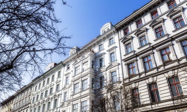Weise Fassaden von Mehrfamilienhäusern in Berlin Kreuzberg im Winter mit blätterlosen Bäumen im Vordergrund und blauem Himmel über den Dächern