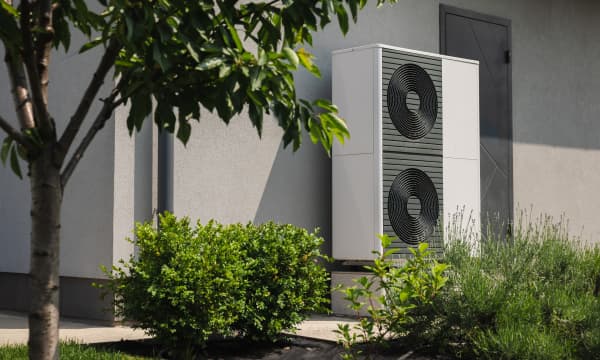 Moderne Wärmepumpen an der Fassade eines Wohnhauses mit grünem Garten