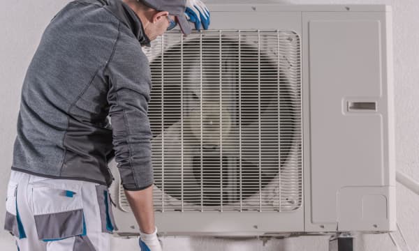 Techniker arbeitet an einer Luft-Wärmepumpe, die vor einem Haus angebracht ist