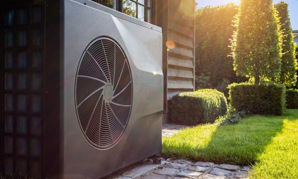 Wärmepumpe im Garten, neben Poolhaus mit Holzfassade an einem sonnigen Tag