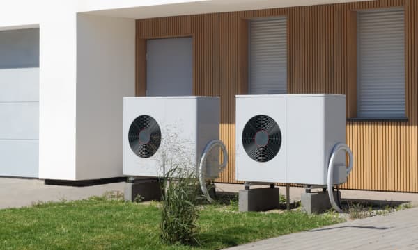 Zwei Luftwärmepumpen auf kleiner Rasenfläche vor Haus mit Holzvertäfelung an der Fassade