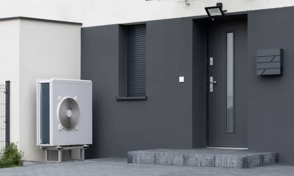 Weiße Luft-Wärmepumpe auf Sockel steht an modernem, dunklem Wohnhaus