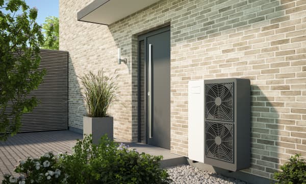 Grau-weiße Wärmepumpe neben der Haustür eines modernen Wohnhauses