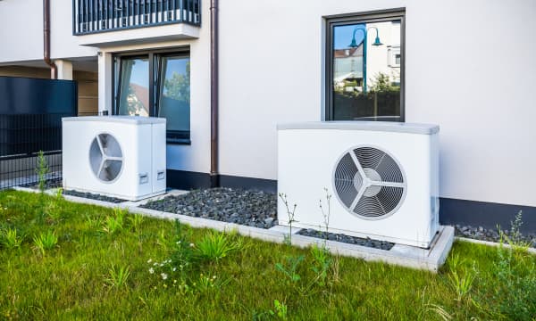 Zwei weiße Wärmepumpen vor weißer Fassade eines Wohngebäudes, davor grünes Gras