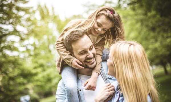 Junges lachendes Paar im Grünen, der Vater hat seine Tochter auf den Schultern