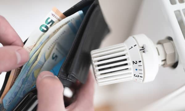 Nahaufnahme einer Geldbörse mit Bargeld neben Thermostat am Heizkörper