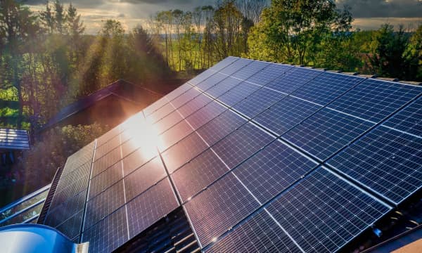 Schrägansicht eines mit Solarmodulen bedeckten Hausdachs. Die Sonne scheint durch bewölkten Himmel auf die Module