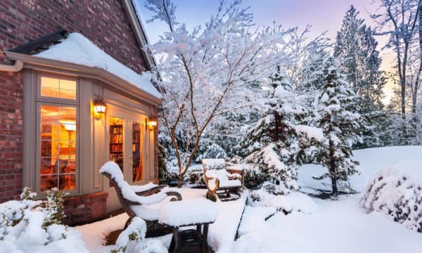 Schneebedeckter Garten und Terrasse, Blick in einen erleuchtetes Wohnzimmer eines Einfamilienhauses