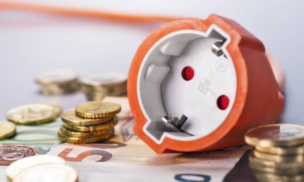 Steckdose mit orangenem Kabel liegt auf Euroscheinen und neben Münzen