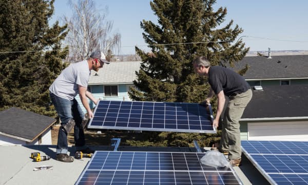 Zwei Arbeiter, die Sonnenkollektoren auf dem Dach eines Wohnhauses installieren.