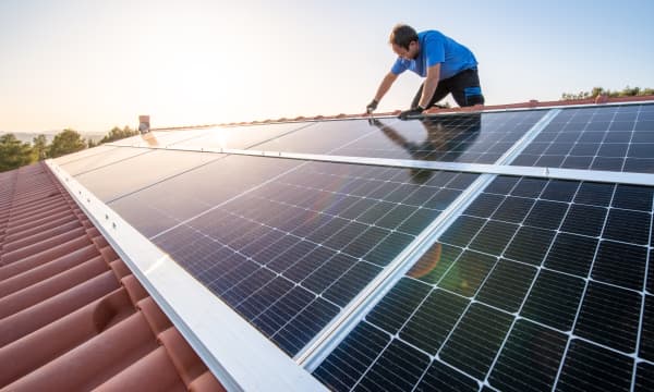 Handwerker installiert Solarmodule auf einem Schrägdach mit Ziegeln bei strahlendem Sonnenschein