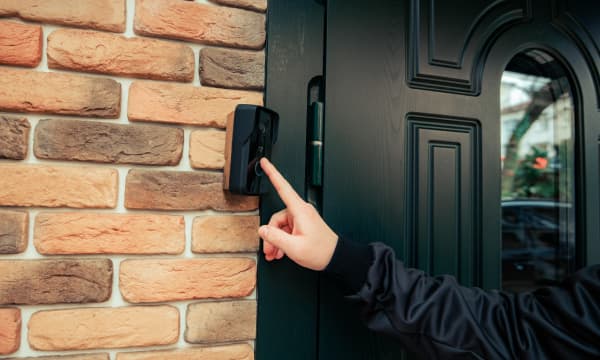 Dunkel gekleidete Person klingelt an der schwarzen Haustür eines Wohnhauses