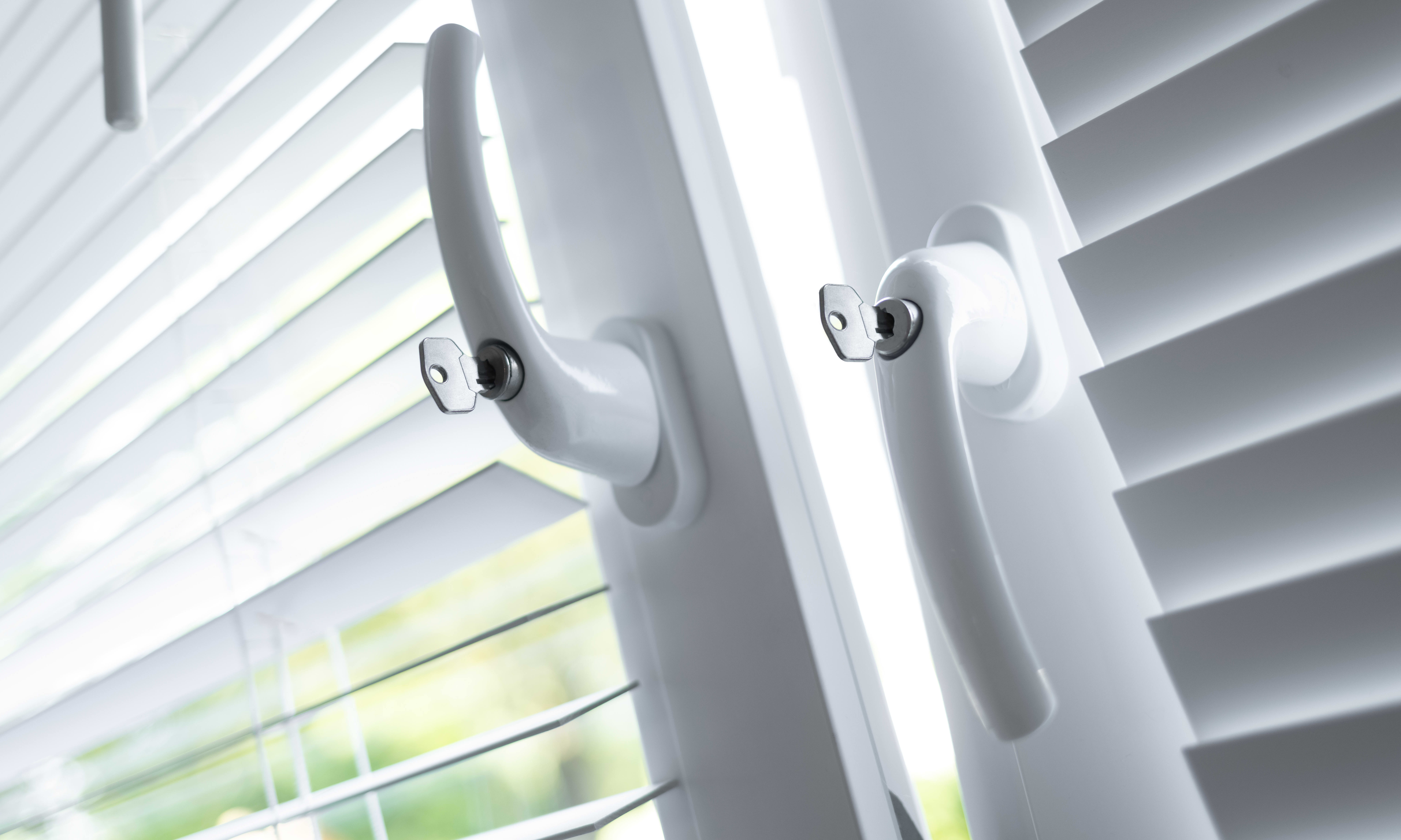 Zwei Fenster mit weißen Rollos und Sicherheitsgriffen, davon ist das linke gekippt