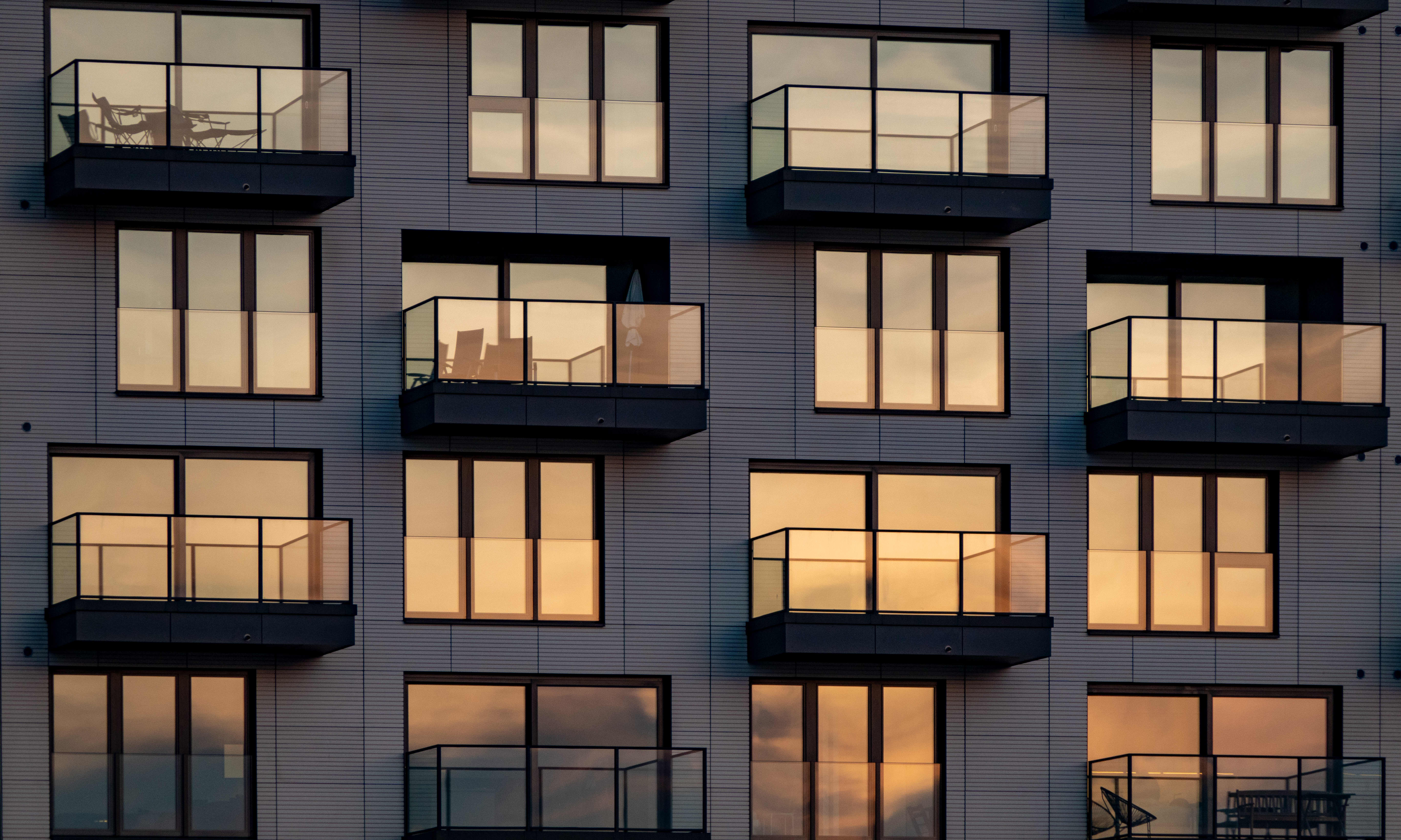 Abendsonne spiegelt sich in Fenstern und Balkonverglasungen an einem modernen Mehrfamilienhaus