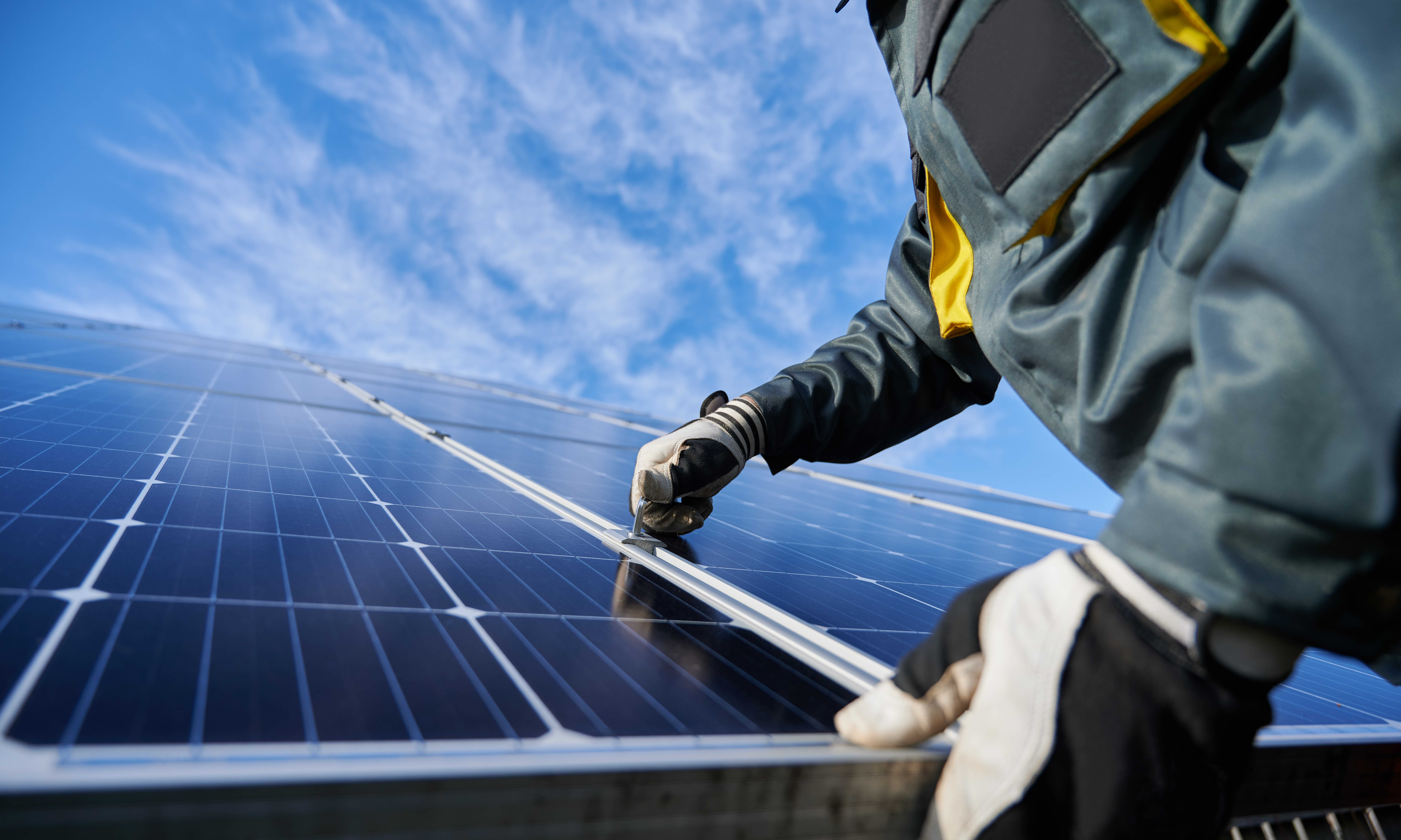 Nahaufnahme eines Arbeiters mit Handschuhen, der an einem installierten Solarmodul auf einem Dach arbeitet