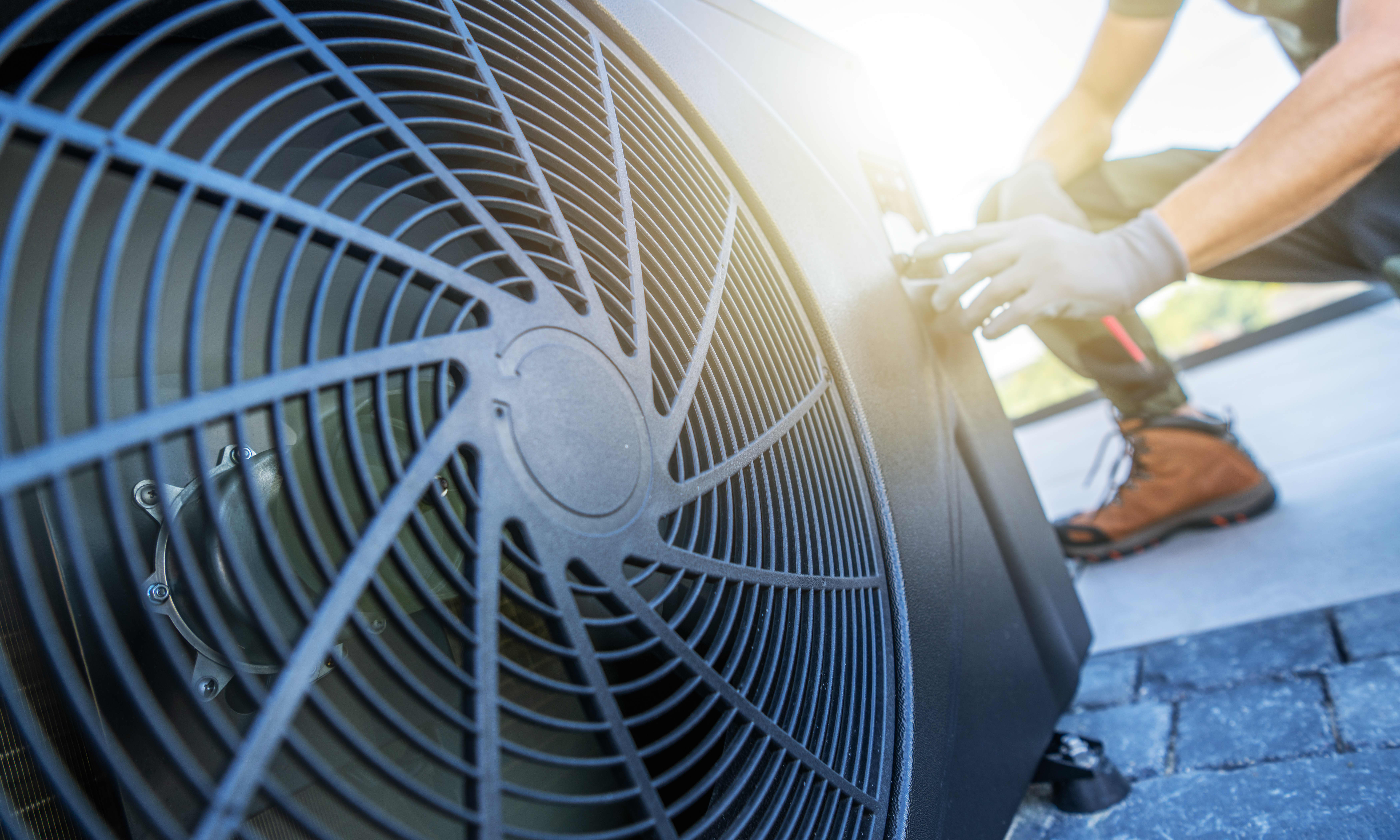Ein Techniker führt Wartungsarbeiten an einer Klimaanlage auf einem Dach durch. Die Sonne scheint hell im Hintergrund