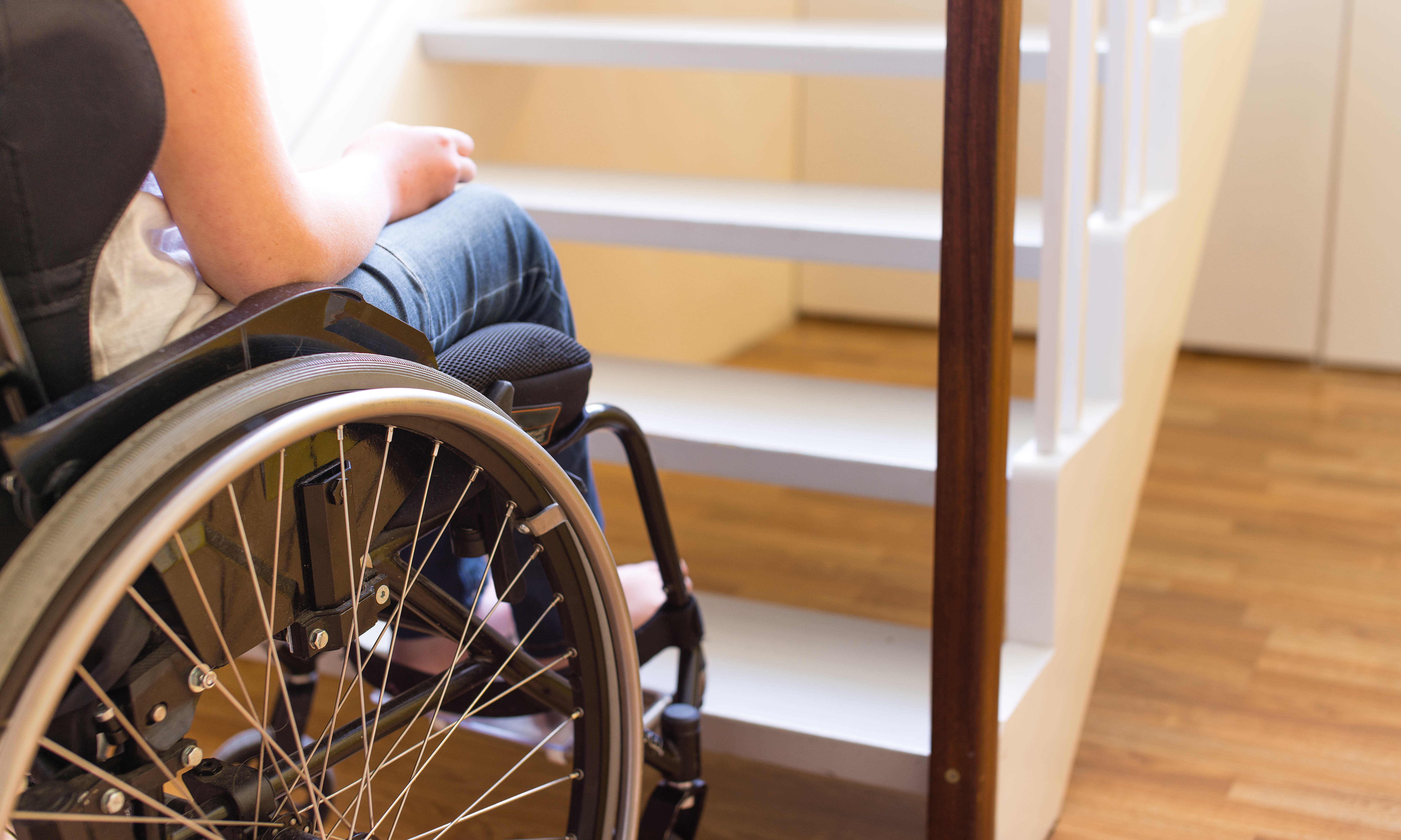 Nahaufnahme einer Person im Rollstuhl am Fuß einer Treppe von hinten