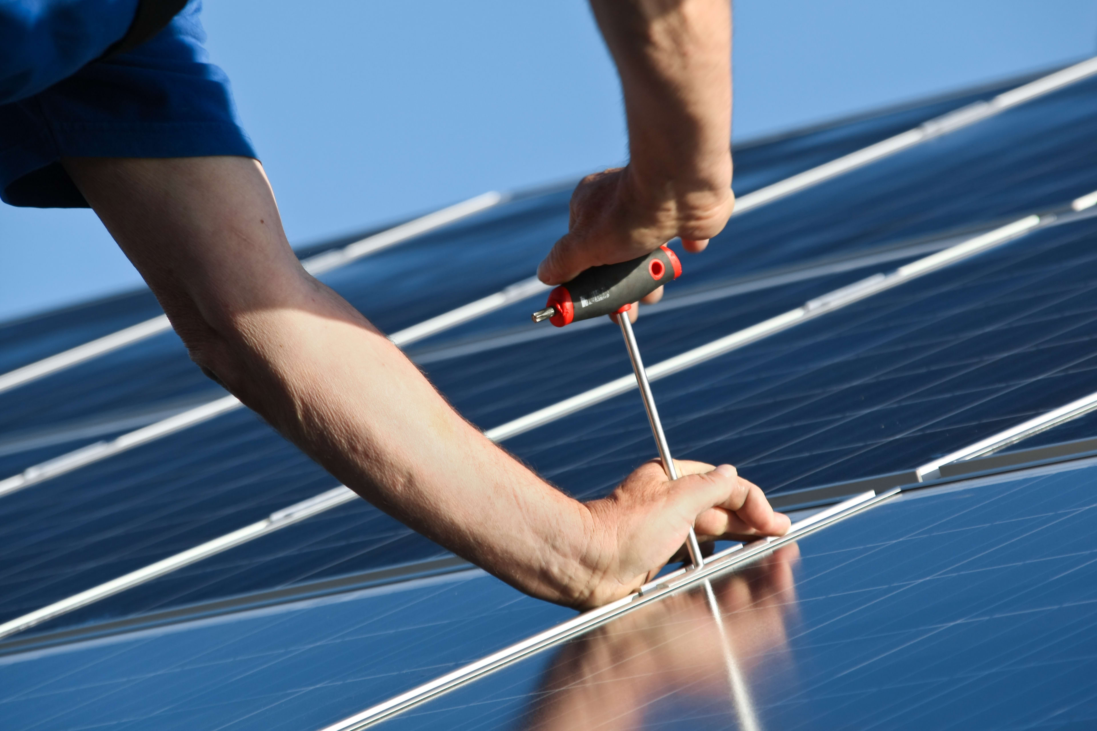Zwei Hände montieren Solarmodule auf einem Dach
