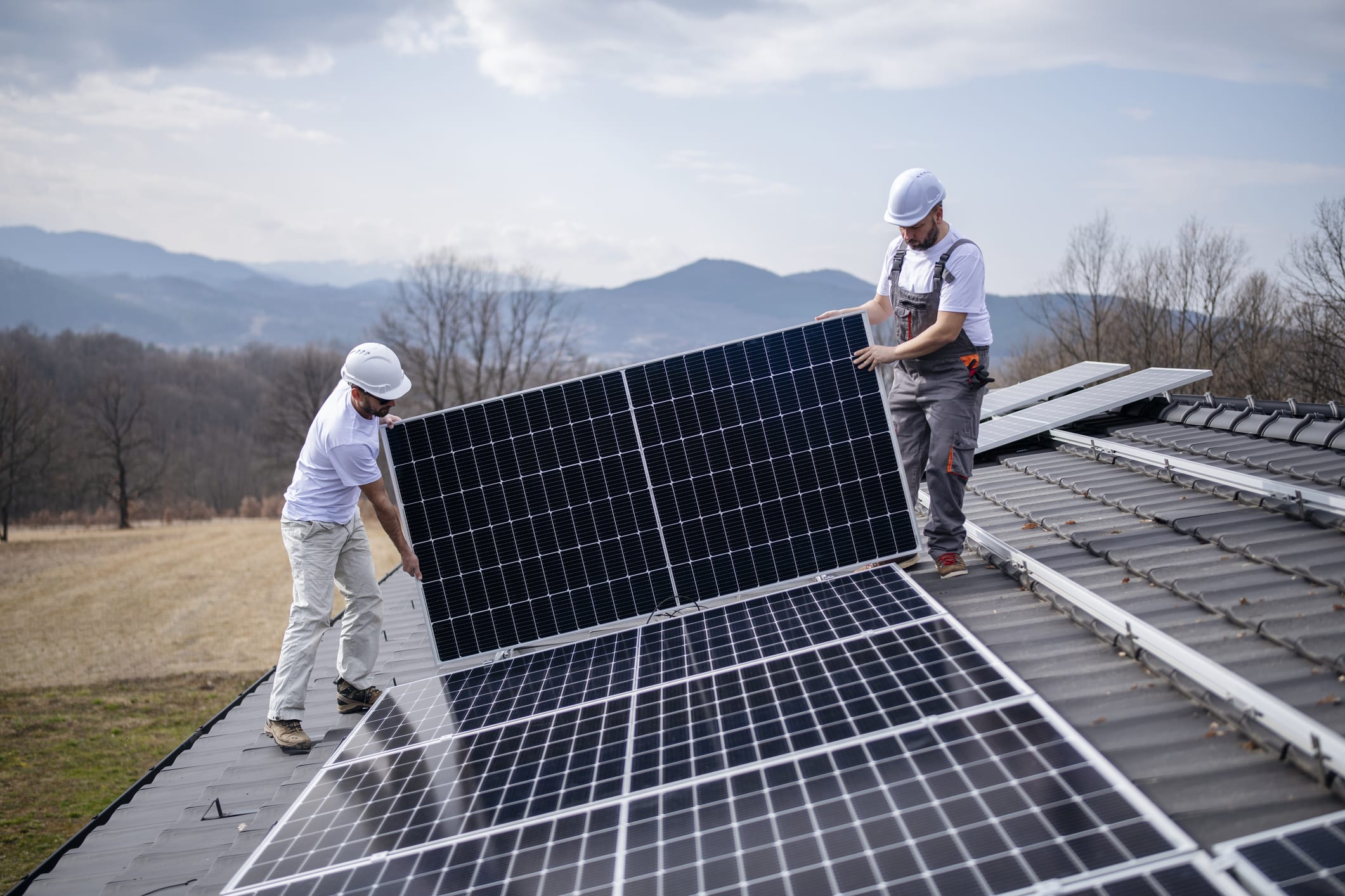 Zwei Installateure montieren ein Solarmodul auf ein Hausdach.