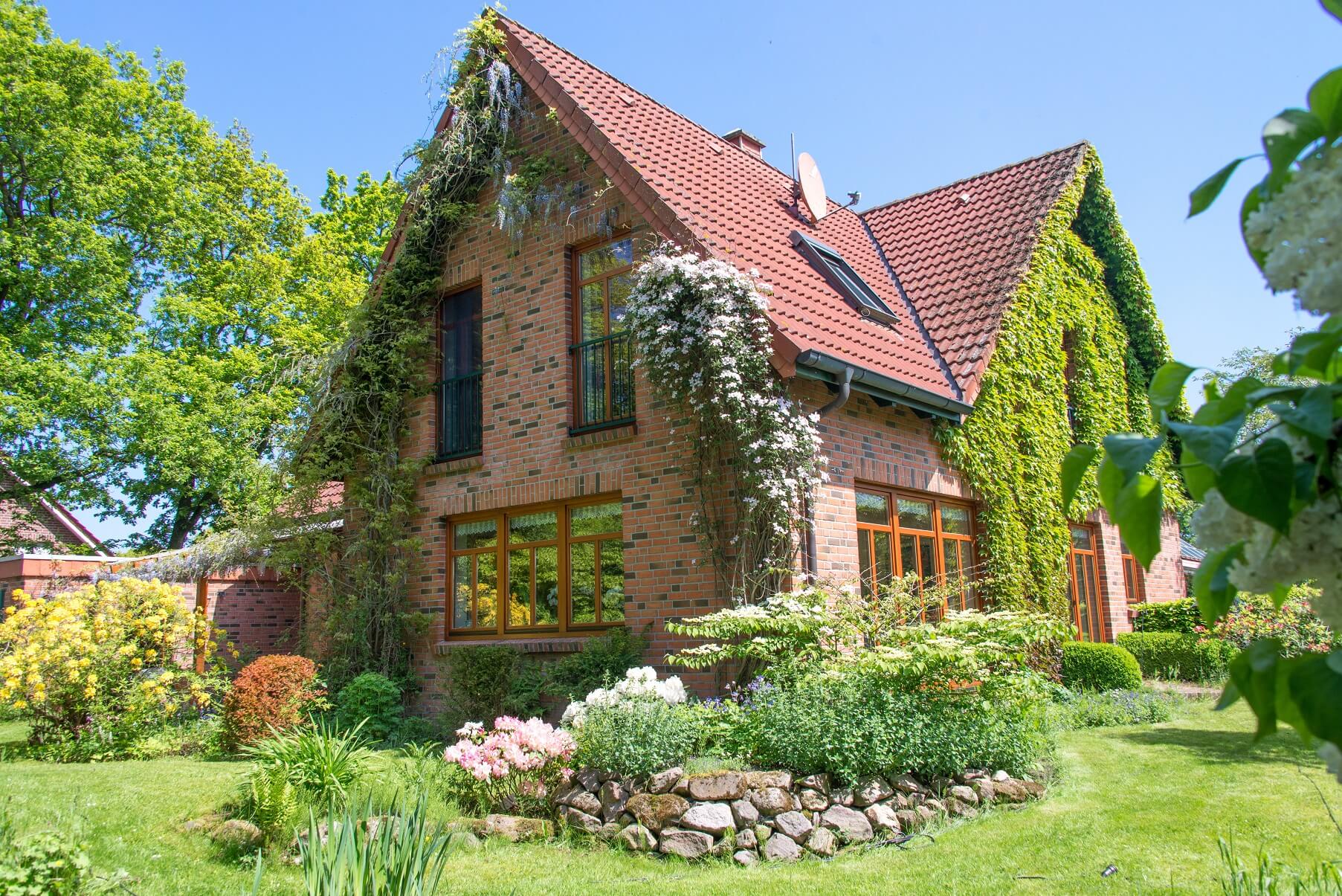 Einfamilienhaus mit Klinkerfassade und roter Dacheindeckung in einem Garten