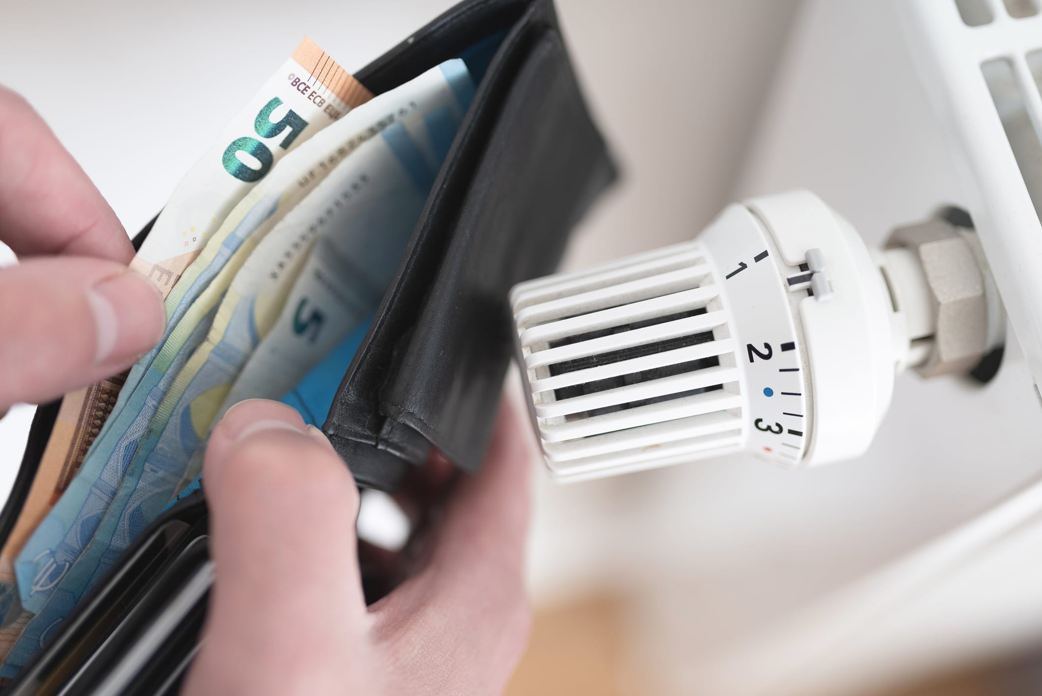 Nahaufnahme einer Geldbörse mit Bargeld neben Thermostat am Heizkörper