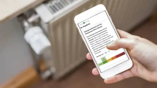 Hand hält Smartphone mit Energieausweis vor Heizkörper