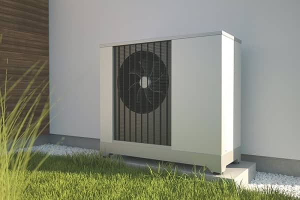 Weiße Luftwärmepumpe vor einer weißen Hauswand