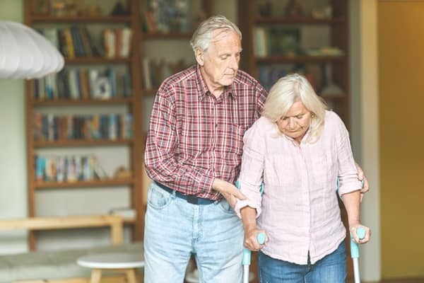 Ältere Frau auf Krücken wird von Mann gestützt