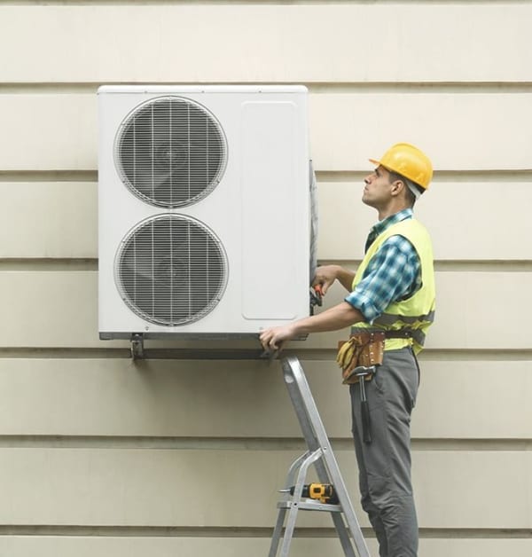 Handwerker bei der Montage einer Wärmepumpe an Hauswand.