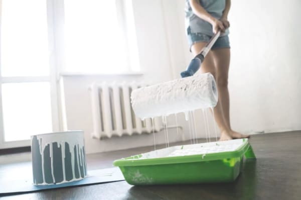 Frau bei Malerarbeiten in einem leeren Raum mit weißen Wänden