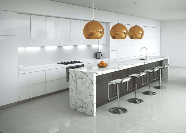Helle, moderne Designküche mit weißer Küchenzeile, großer Marmoroptik-Insel, vier Barhockern und drei goldfarbenen Pendelleuchten.