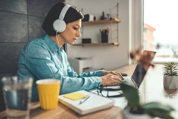Frau sitzt am Schreibtisch mit Laptop und Kopfhörern auf